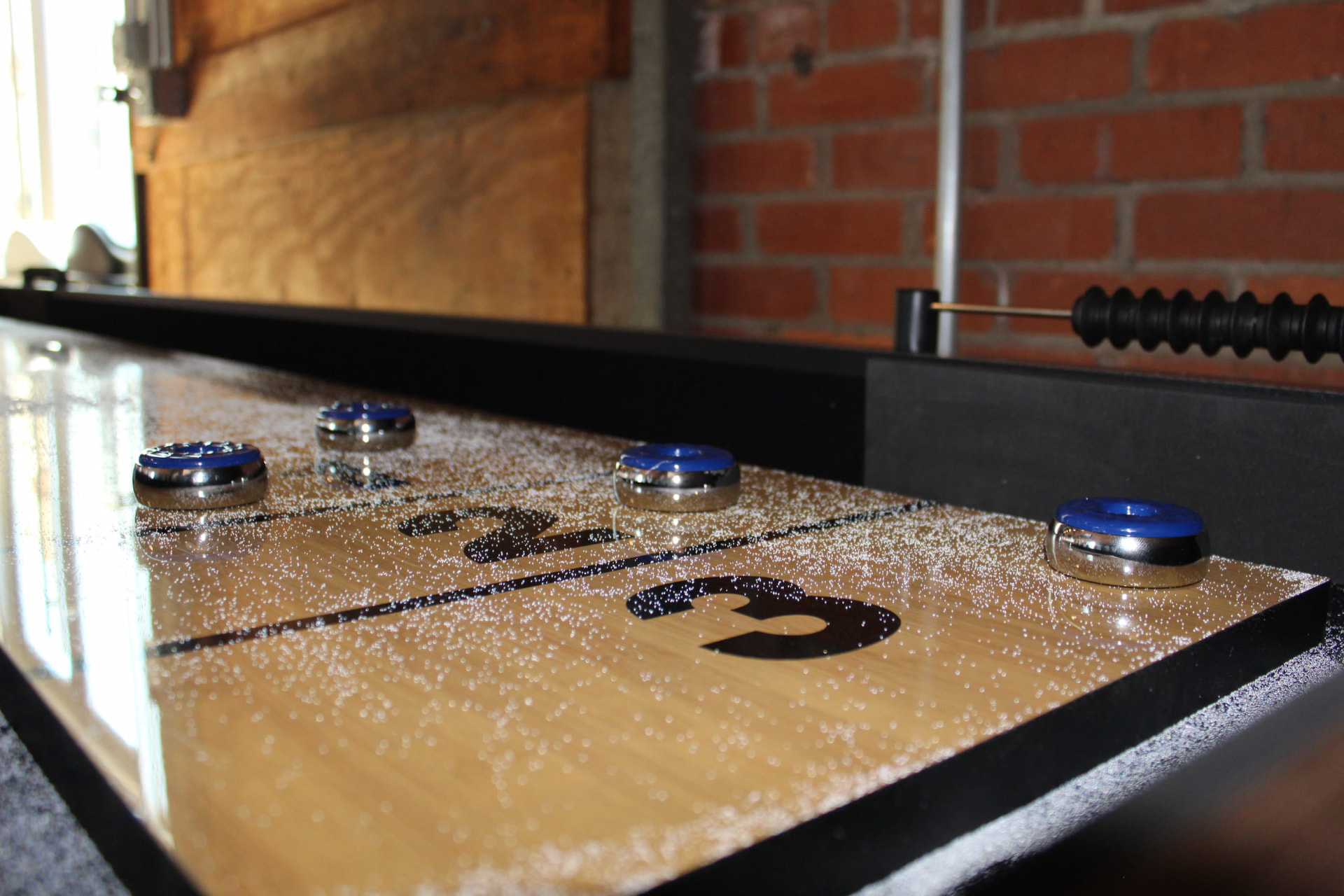 Shuffleboard table with blue pucks against an exposed brick wall