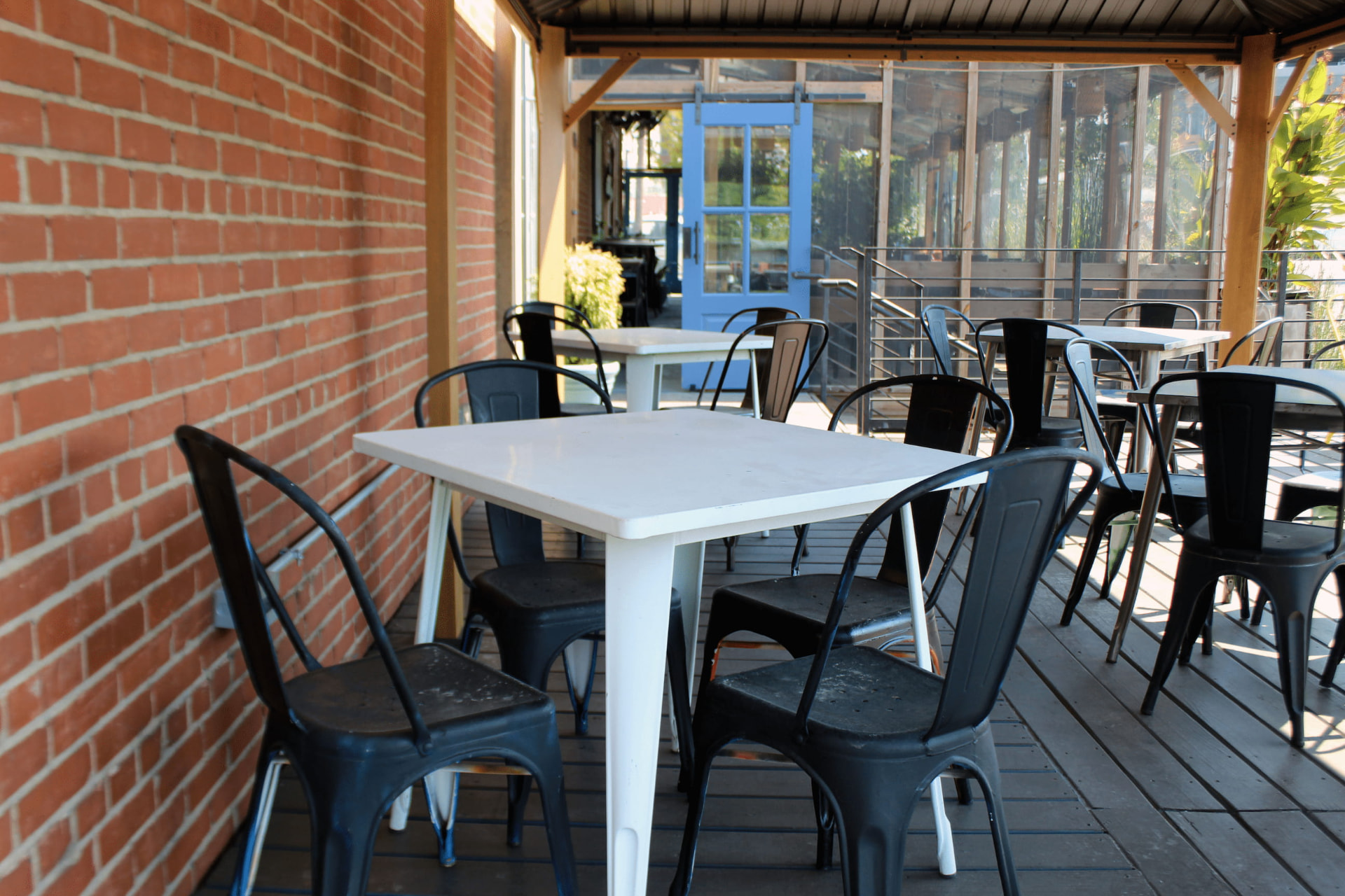 Outdoor patio tables and black metal chairs along a red brick wall